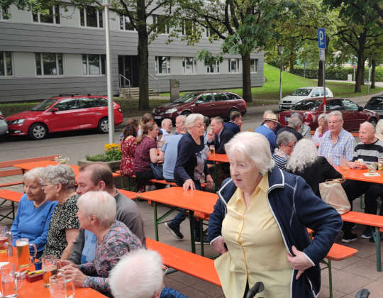 Das Bild zeigt die Bewohner des Wohnstifts beim Sommerfest. Dazu wurden Bierbänke im Hof vor dem Gebäude aufgebaut.